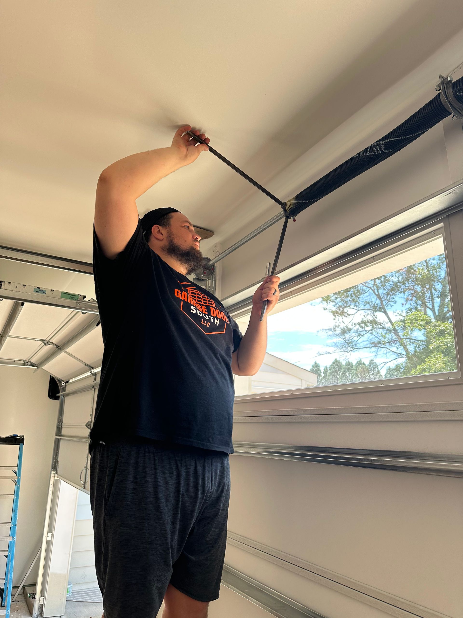 Person adjusting a black garage door seal near a blue wall panel