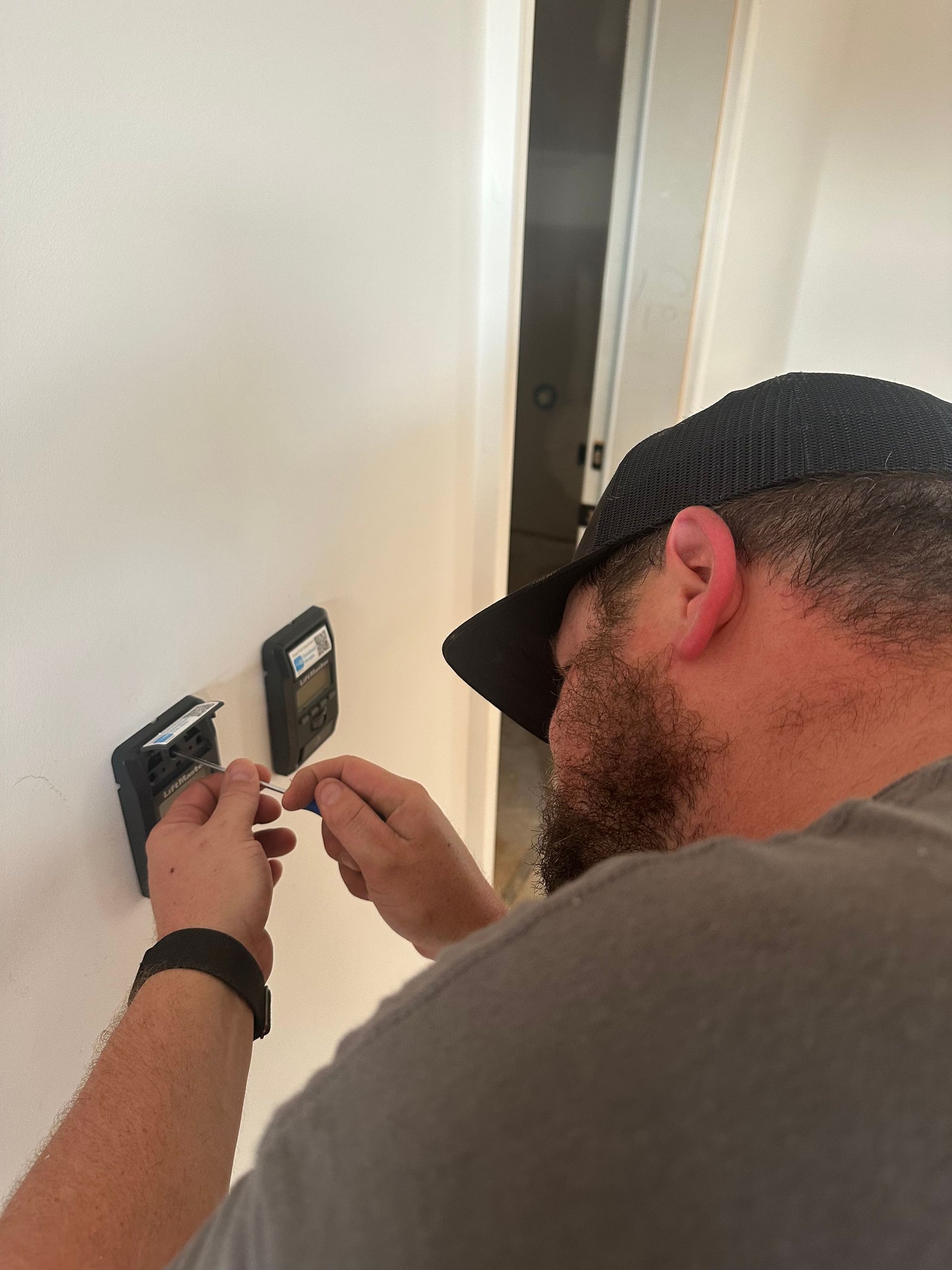 Person using a red-handled tool to adjust a black garage door spring mechanism