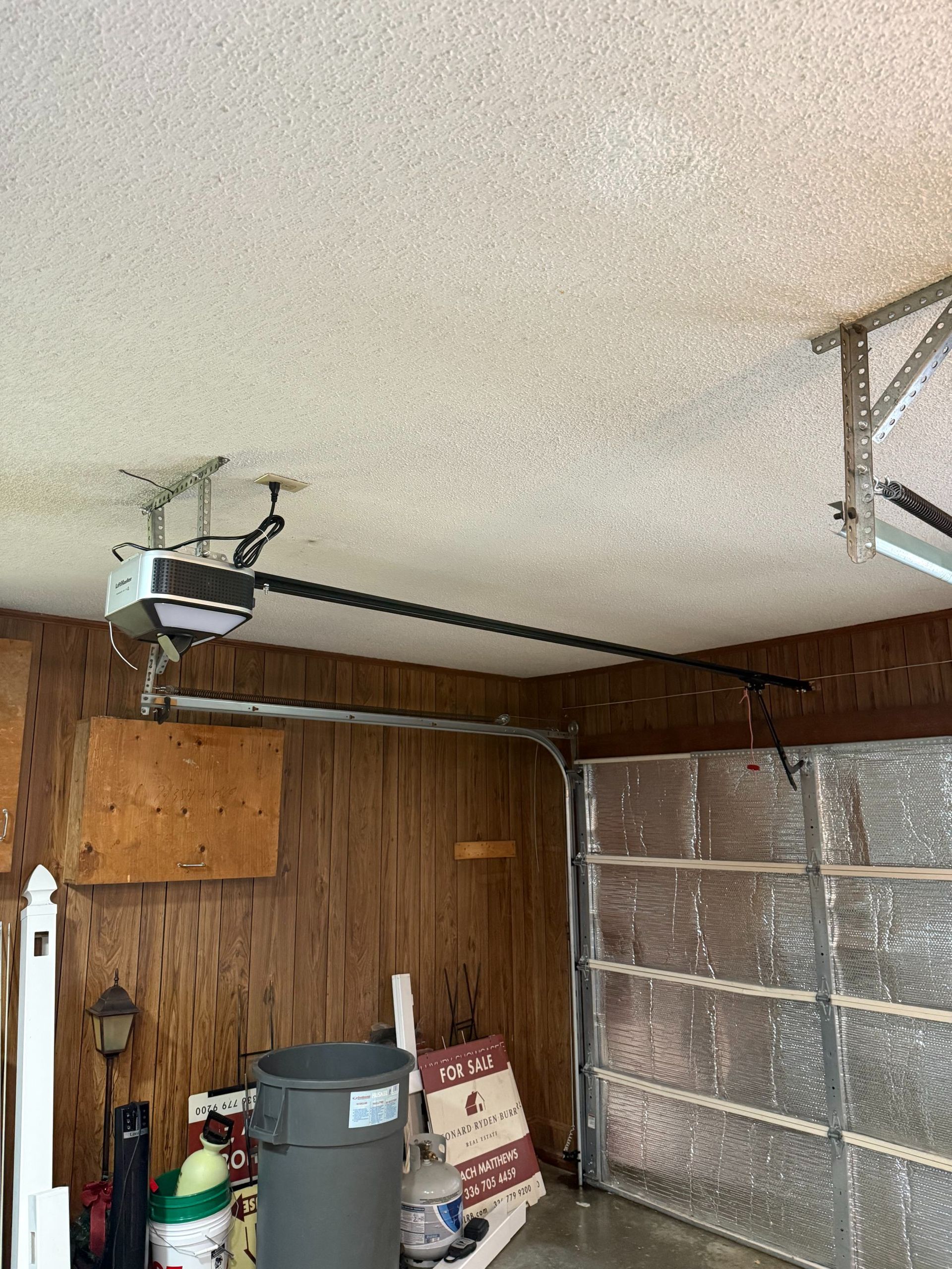 Garage interior with wood-paneled walls, closed garage door, and overhead opener ceiling-mounted.