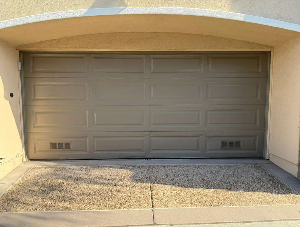 Closed beige garage door under a stucco archway, with a gravel driveway in front.