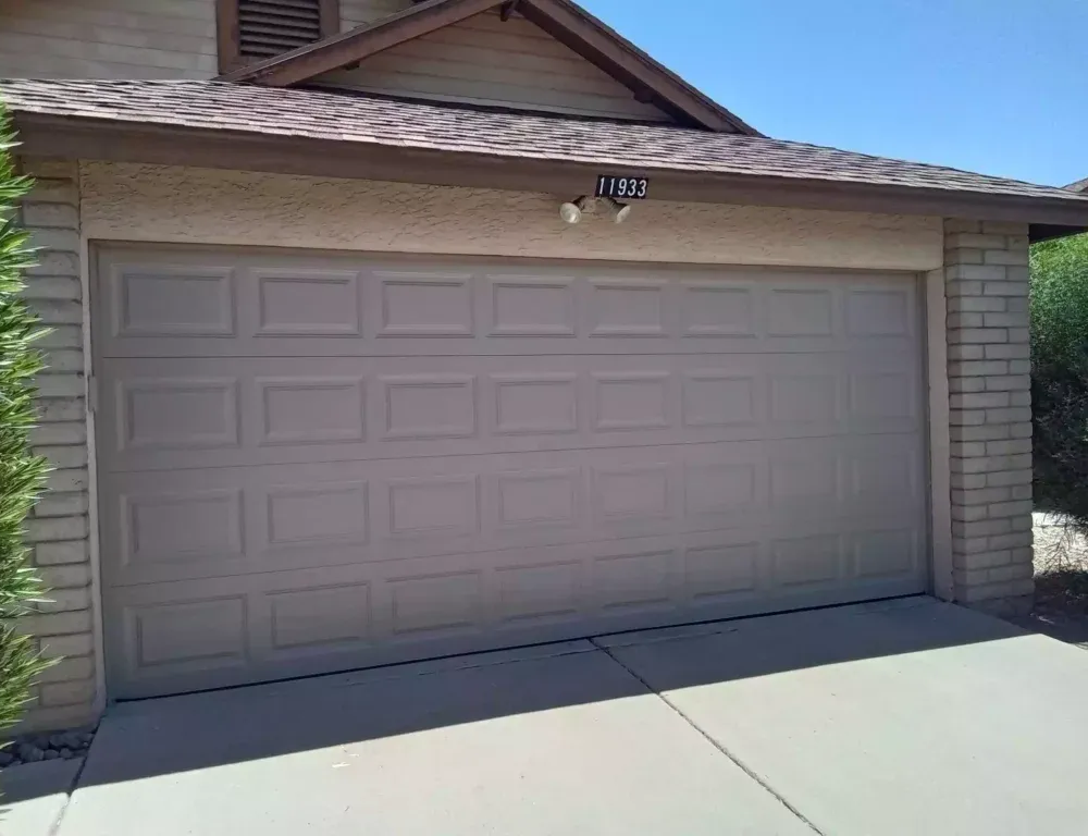 Closed beige two-car garage with a driveway and house exterior in bright sunlight