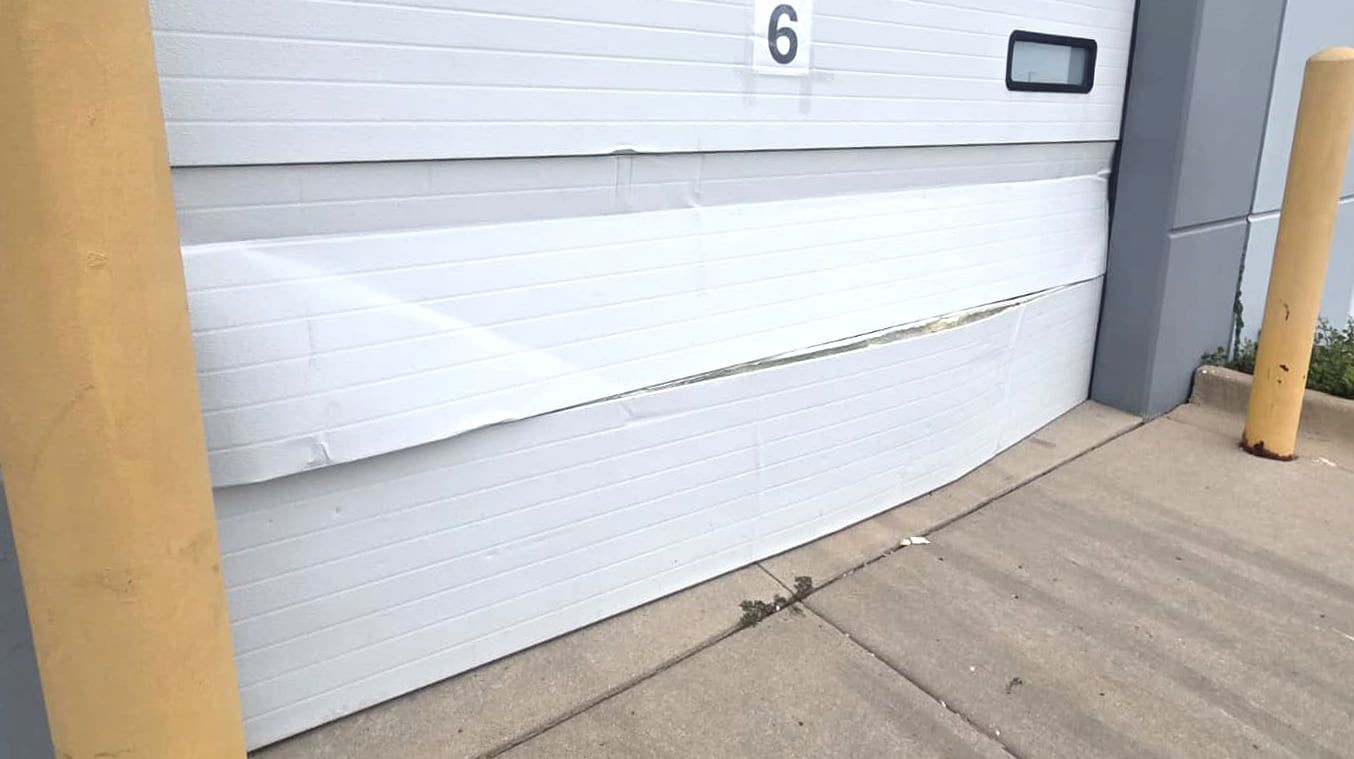Number 6 on a white wall with yellow posts beside a concrete sidewalk.
