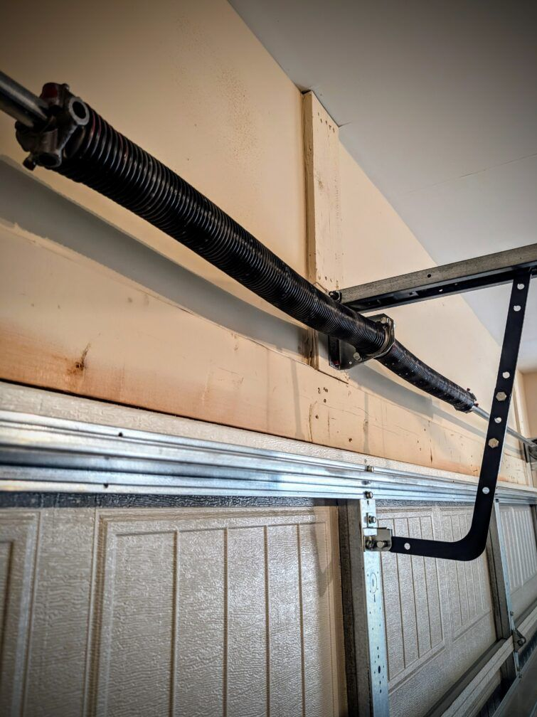 Garage door spring and track mechanism mounted above a paneled door in a beige garage.