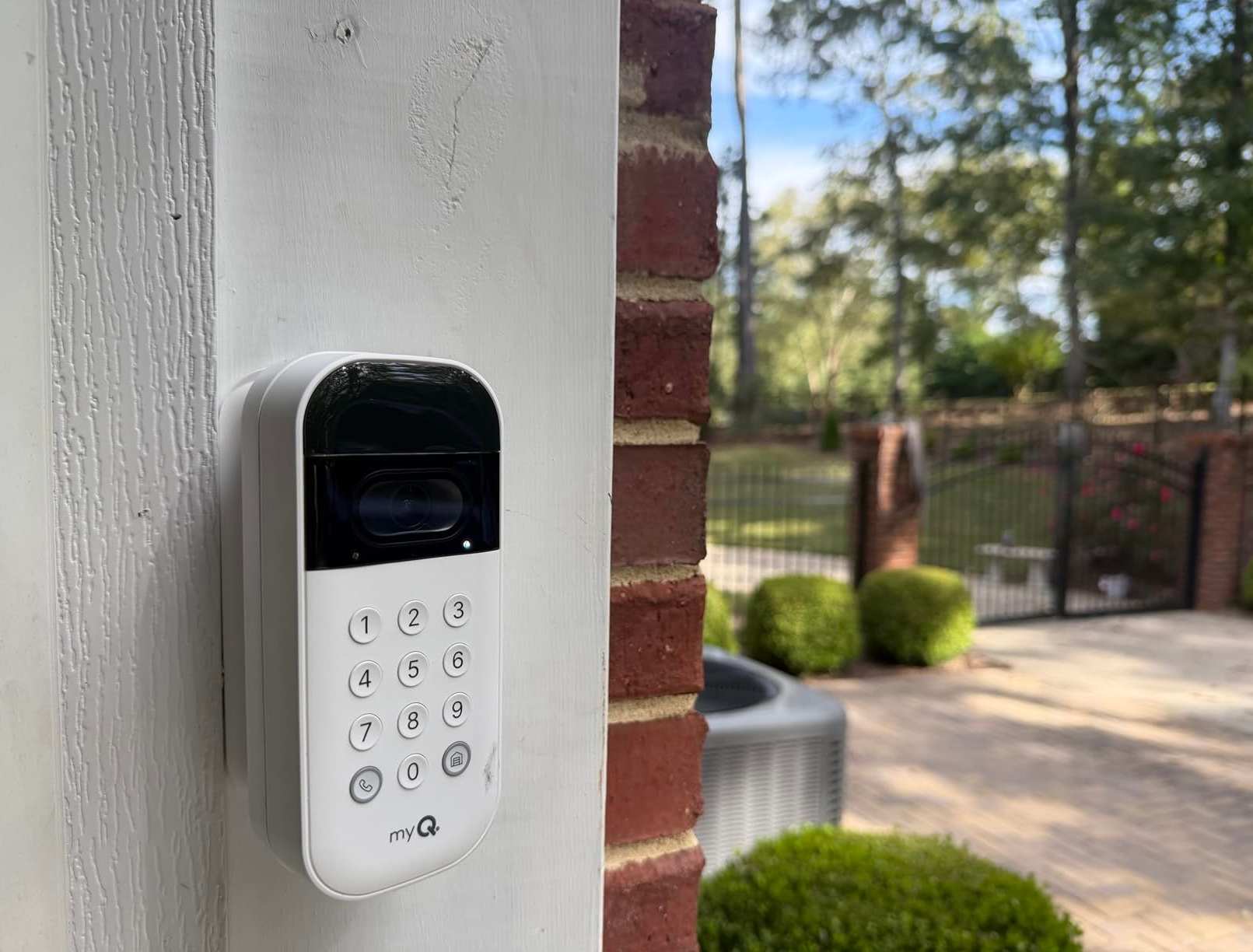 White door keypad lock mounted on a porch wall beside a brick column and yard