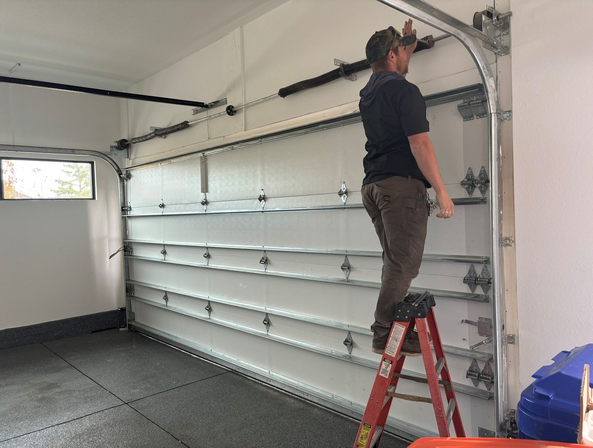 Person standing on a ladder inspecting a garage door opener in a white garage