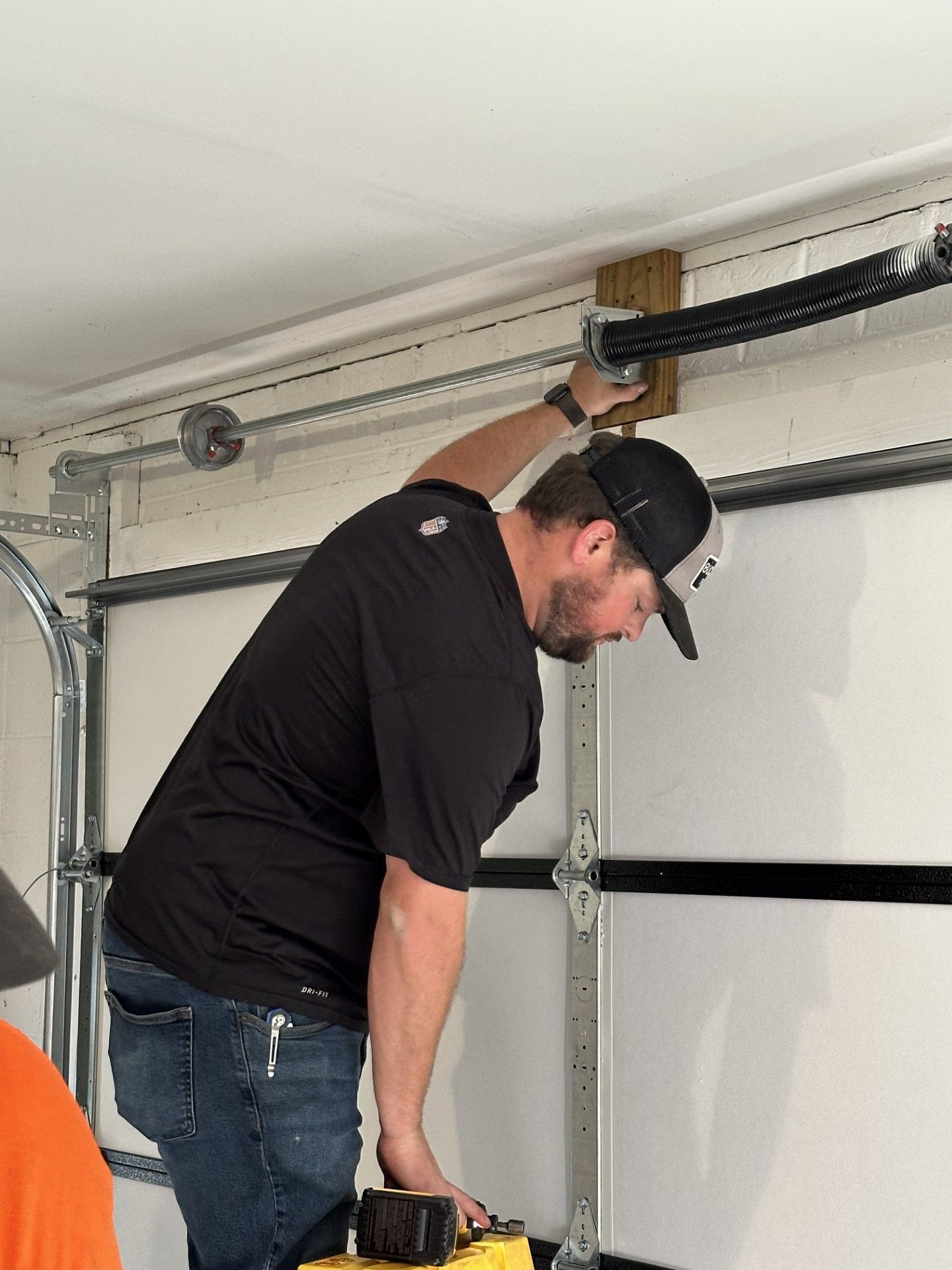 Close-up of a garage door corner with black hardware, white paneling, and a damaged wall edge.