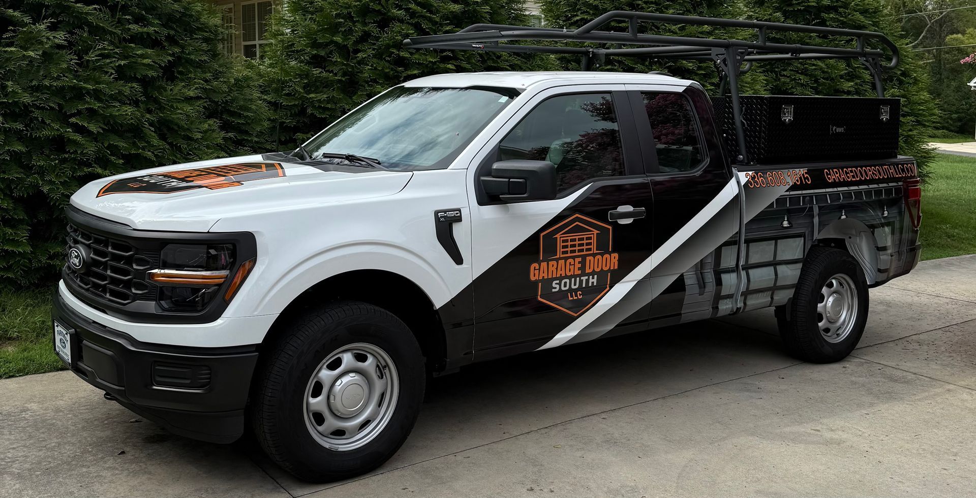 White and black utility pickup truck with roof rack and side logo, parked outdoors on a paved lot