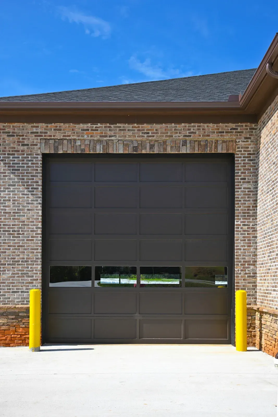 Closed dark gray garage door on a brick building with yellow bollards in front