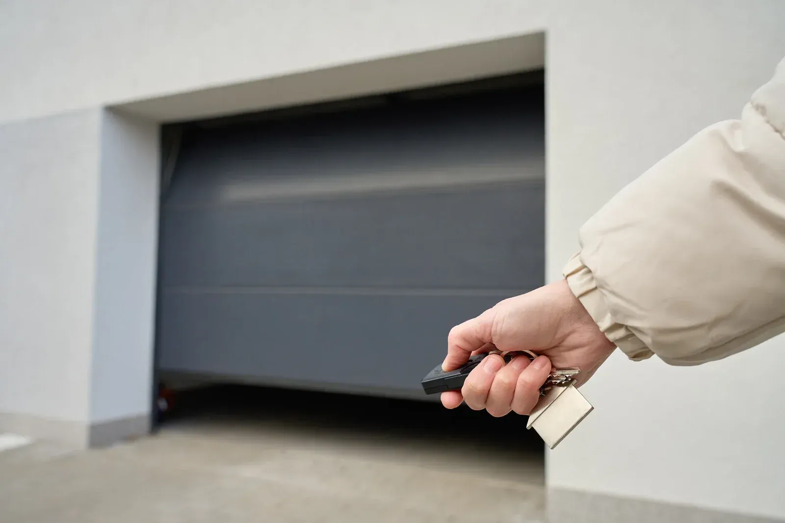 Hand holding a car key fob toward a closed garage door