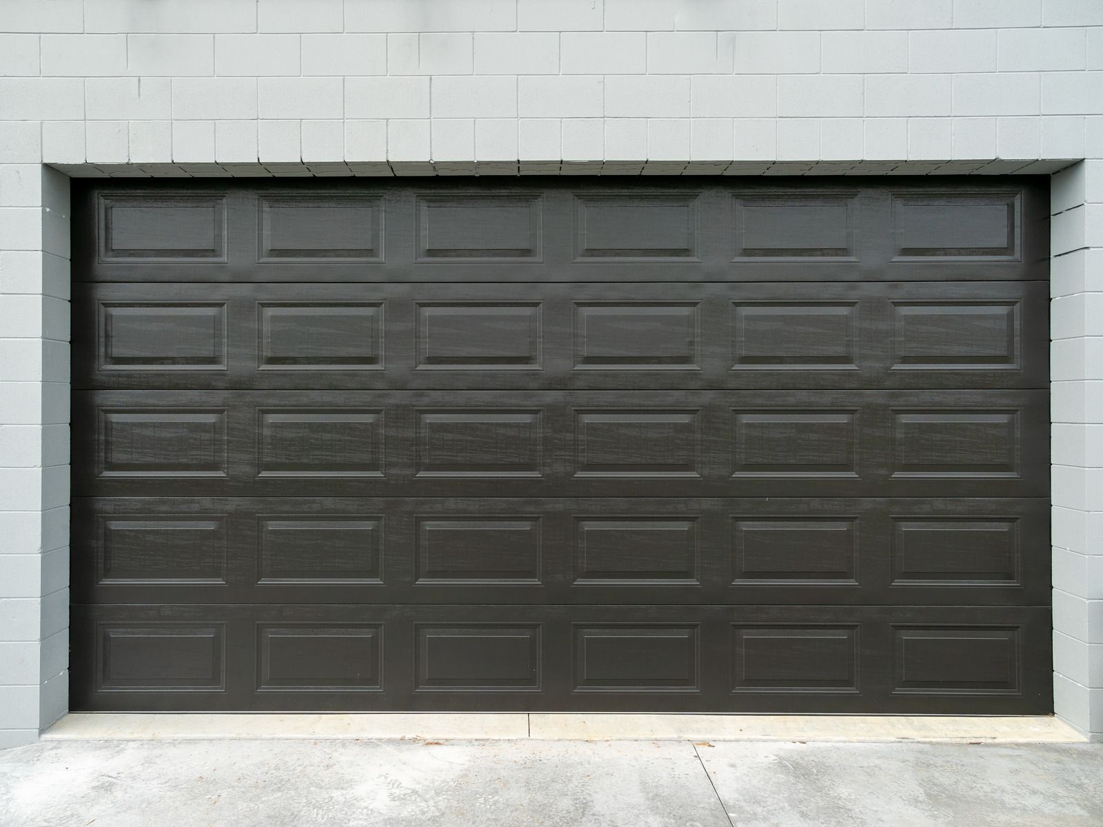 Dark gray garage door set in a light gray brick wall