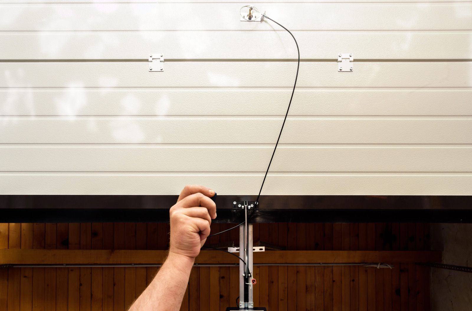 Hand raising a curved antenna or microphone stand against a lined white wall and wooden paneling
