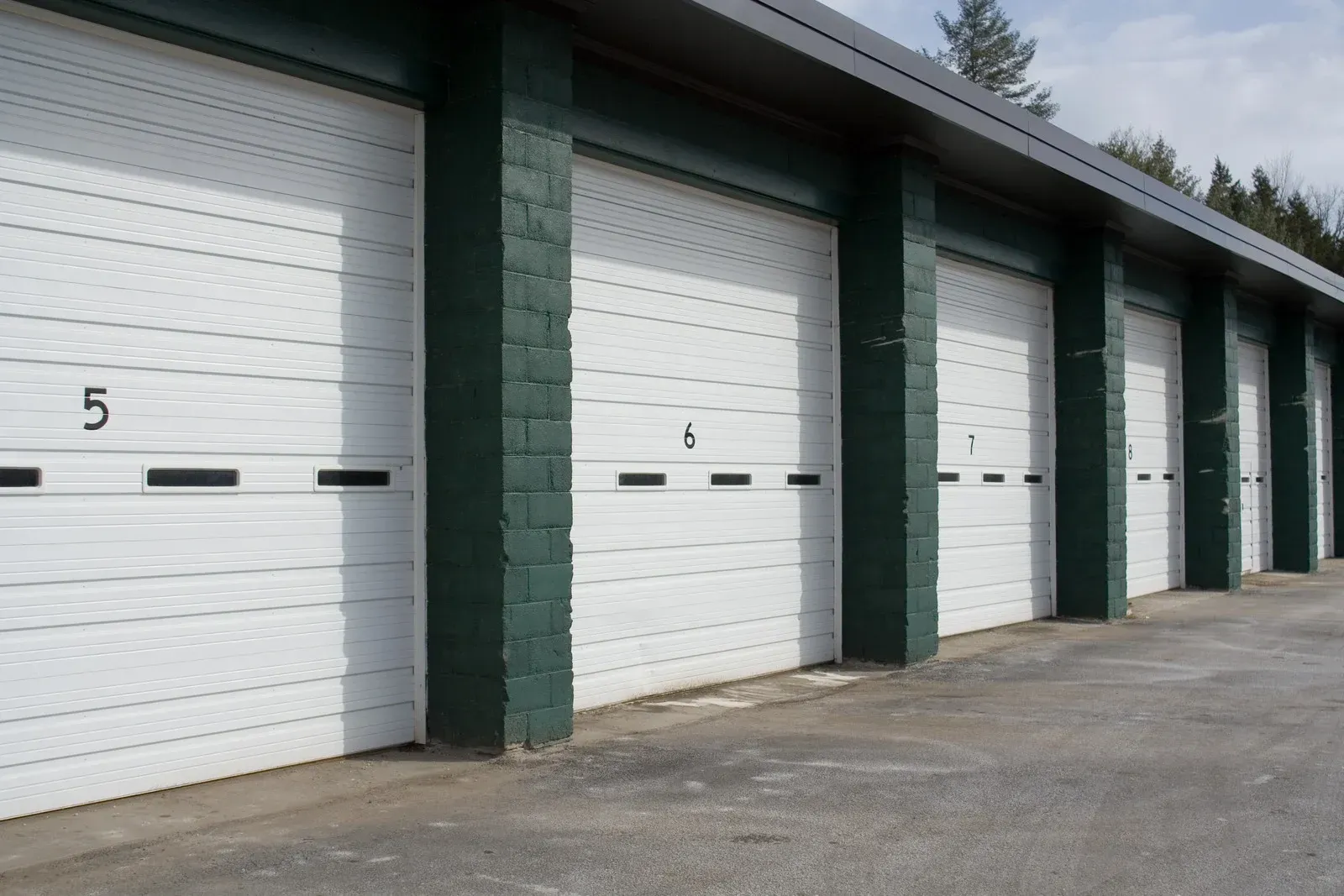 Row of white garage doors with green pillars in a storage unit building