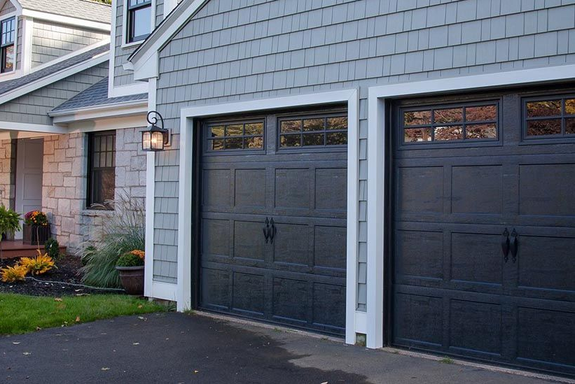 Two black garage doors on a gray house with white trim and a driveway