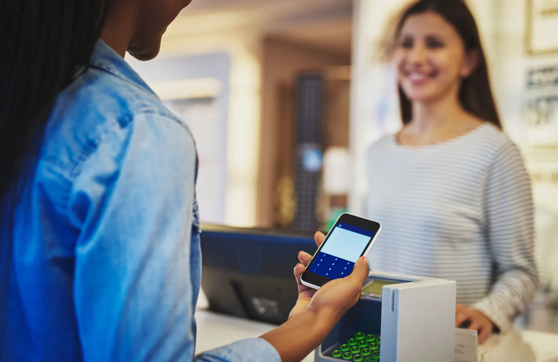 Customer paying with smartphone at a store counter while cashier smiles in the background