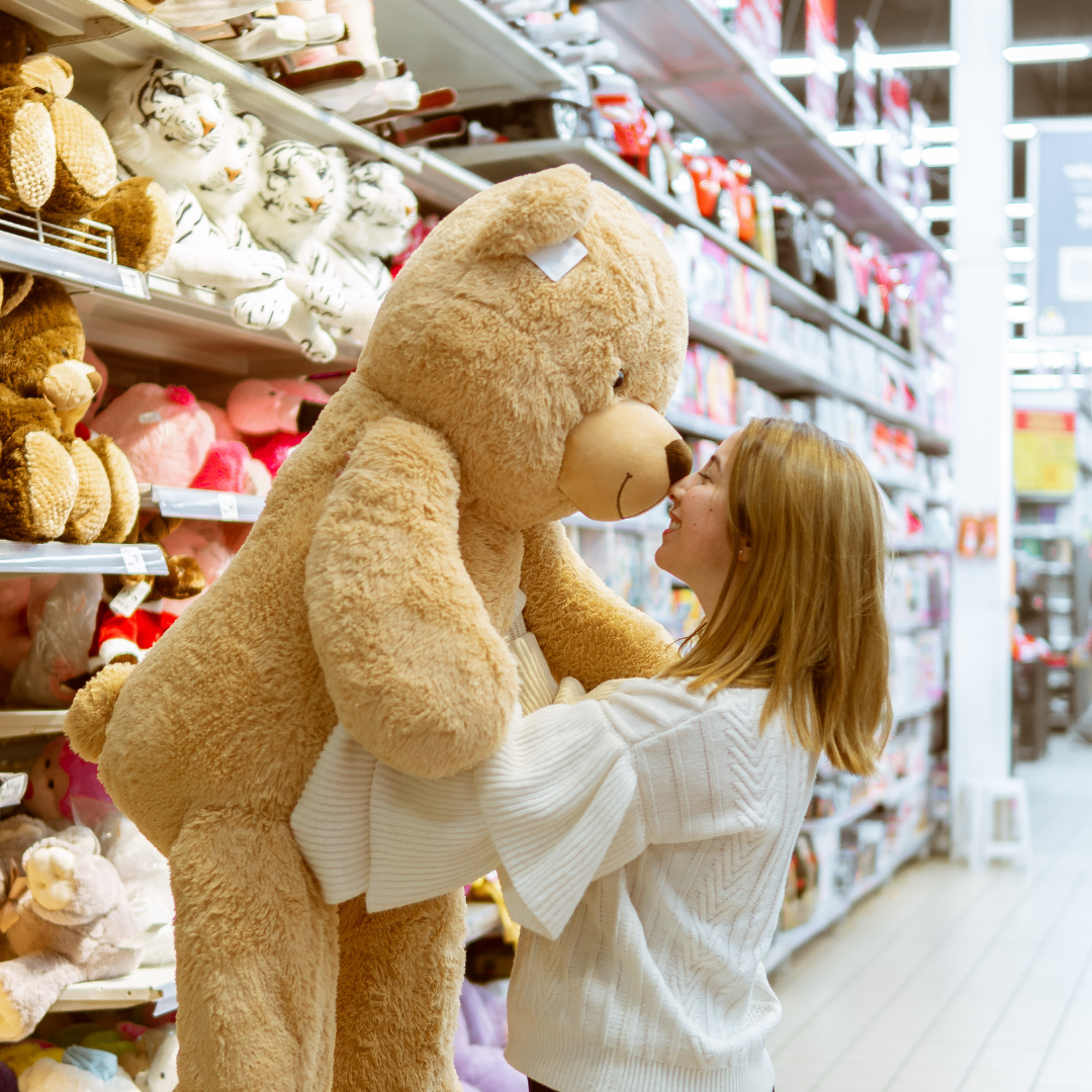 Brinquedos é com o ConnectStore. Uma mulher está segurando um grande ursinho de pelúcia em uma loja.