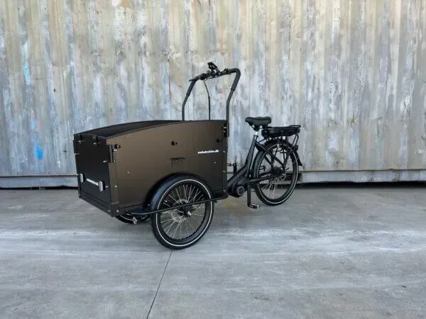 Sort ladcykel parkeret på en murstenssti med en gul bygning i baggrunden.