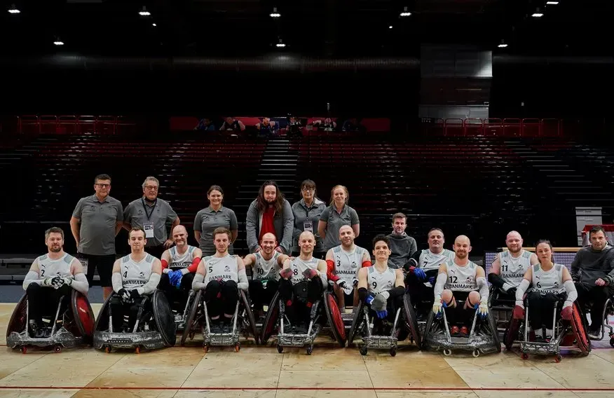 Kørestolsrugbyhold poserer til et gruppebillede i en indendørs arena.