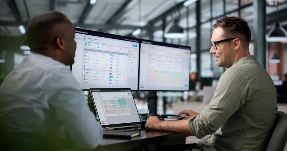 Two coworkers reviewing data on multiple monitors in a modern office workspace