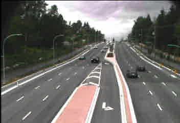 Aerial view of a multi-lane highway with a red bus lane and cars under a cloudy sky.