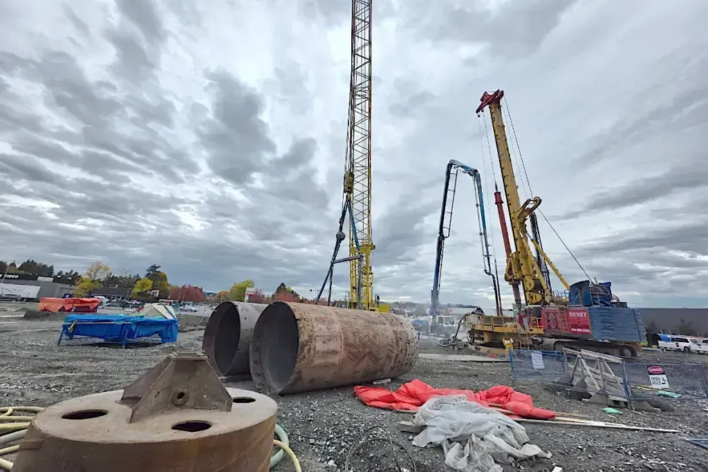 Construction site with cranes lifting large steel pipes under a cloudy sky