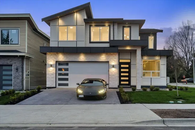 Modern two-story house at dusk with lit windows, garage, and a car parked in the driveway
