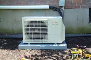 A white fujitsu air conditioner is sitting on top of a metal block next to a brick wall.