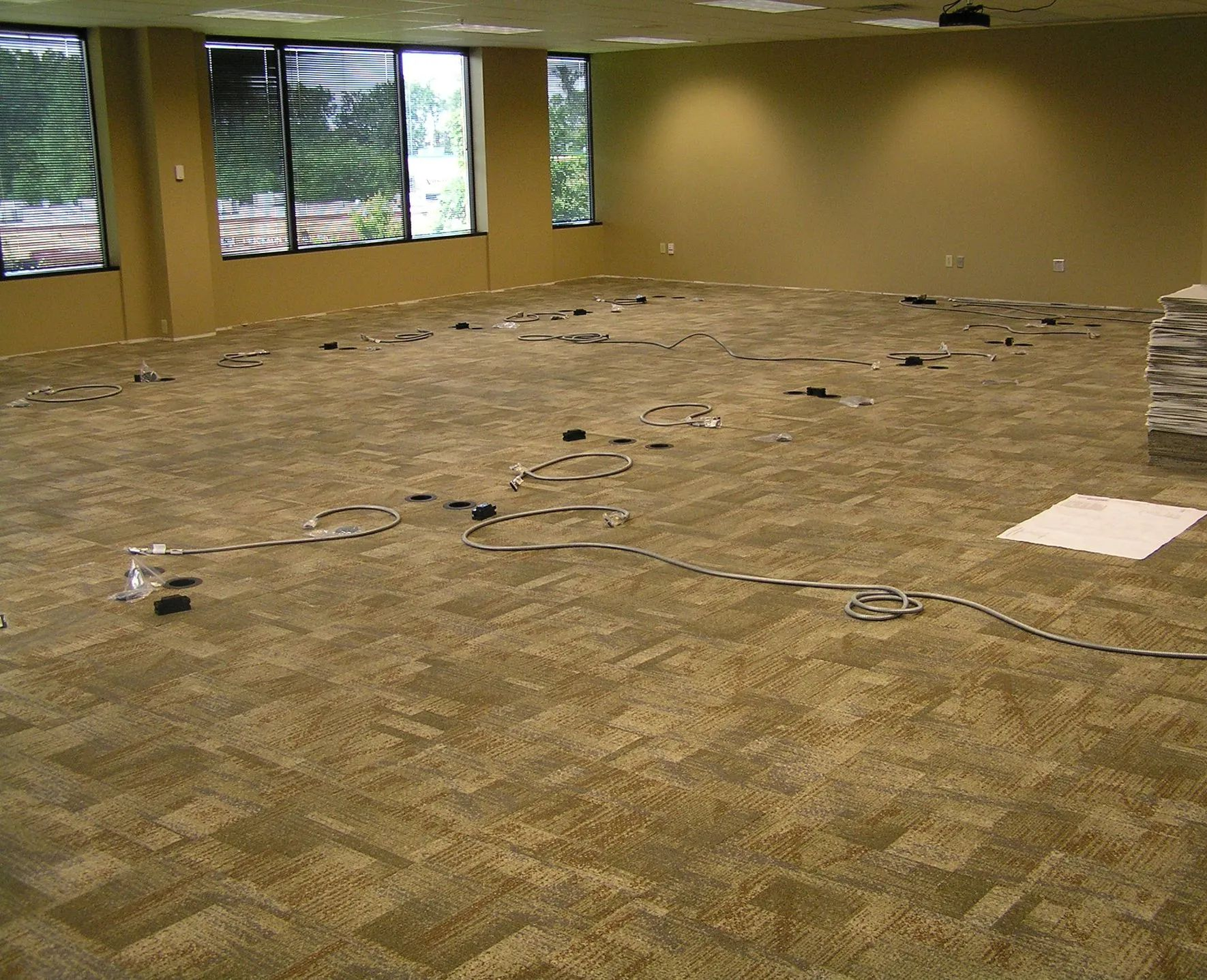 Empty office room with beige carpet removed in patches and cables scattered across the floor