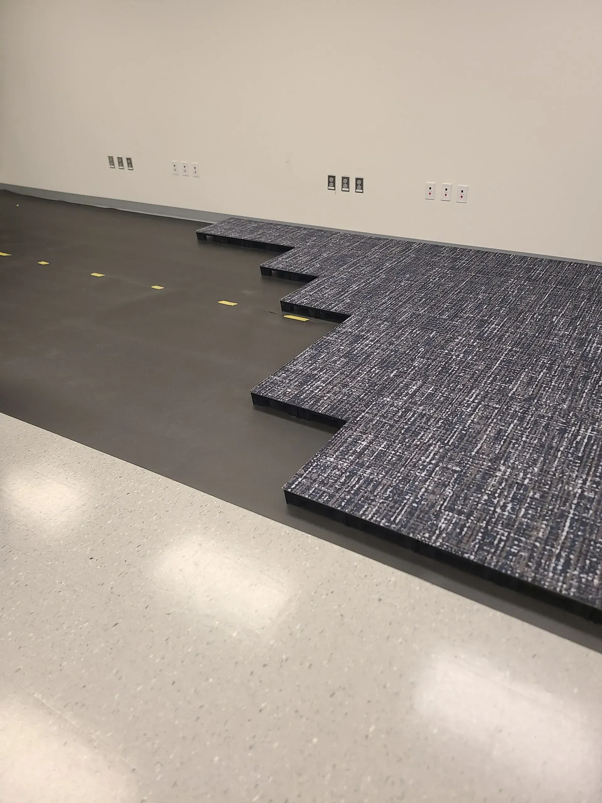 Interlocking dark gray floor mats edge a white wall in a sparse room.