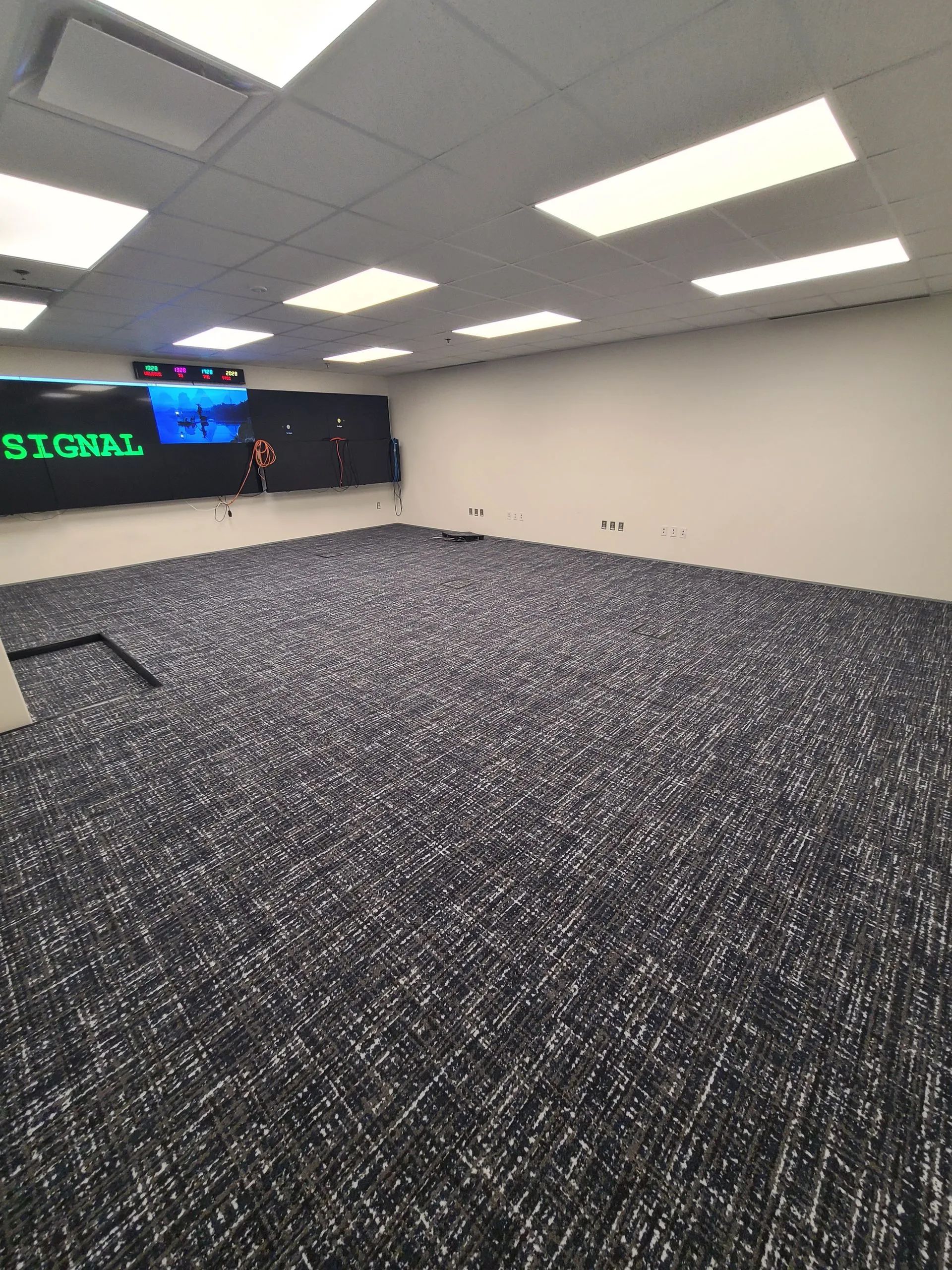 Empty room with dark patterned carpet, large screen displaying text, and ceiling lights.
