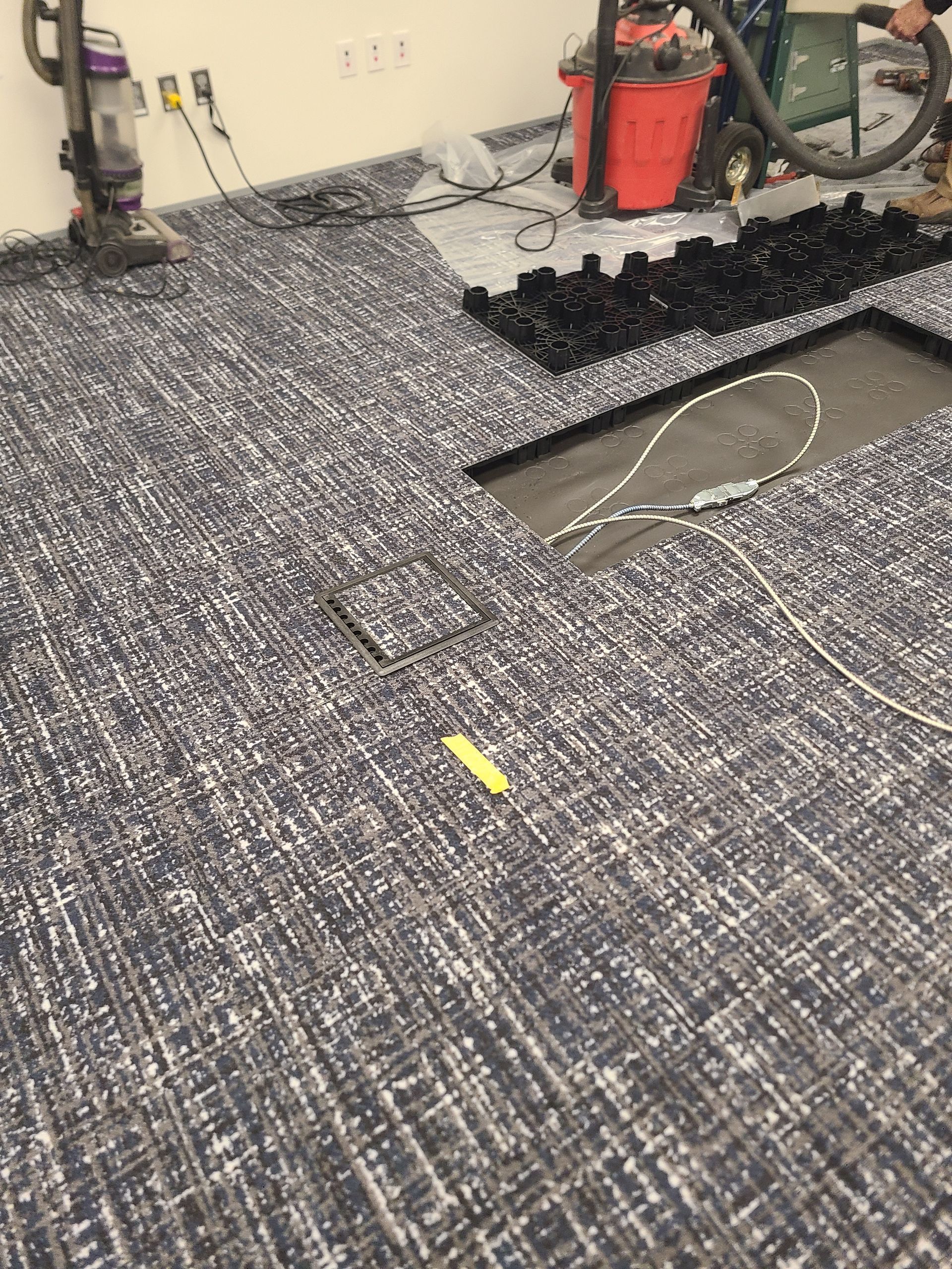 Carpeted floor in a workshop with a large damaged or cut-out section exposing the subfloor.