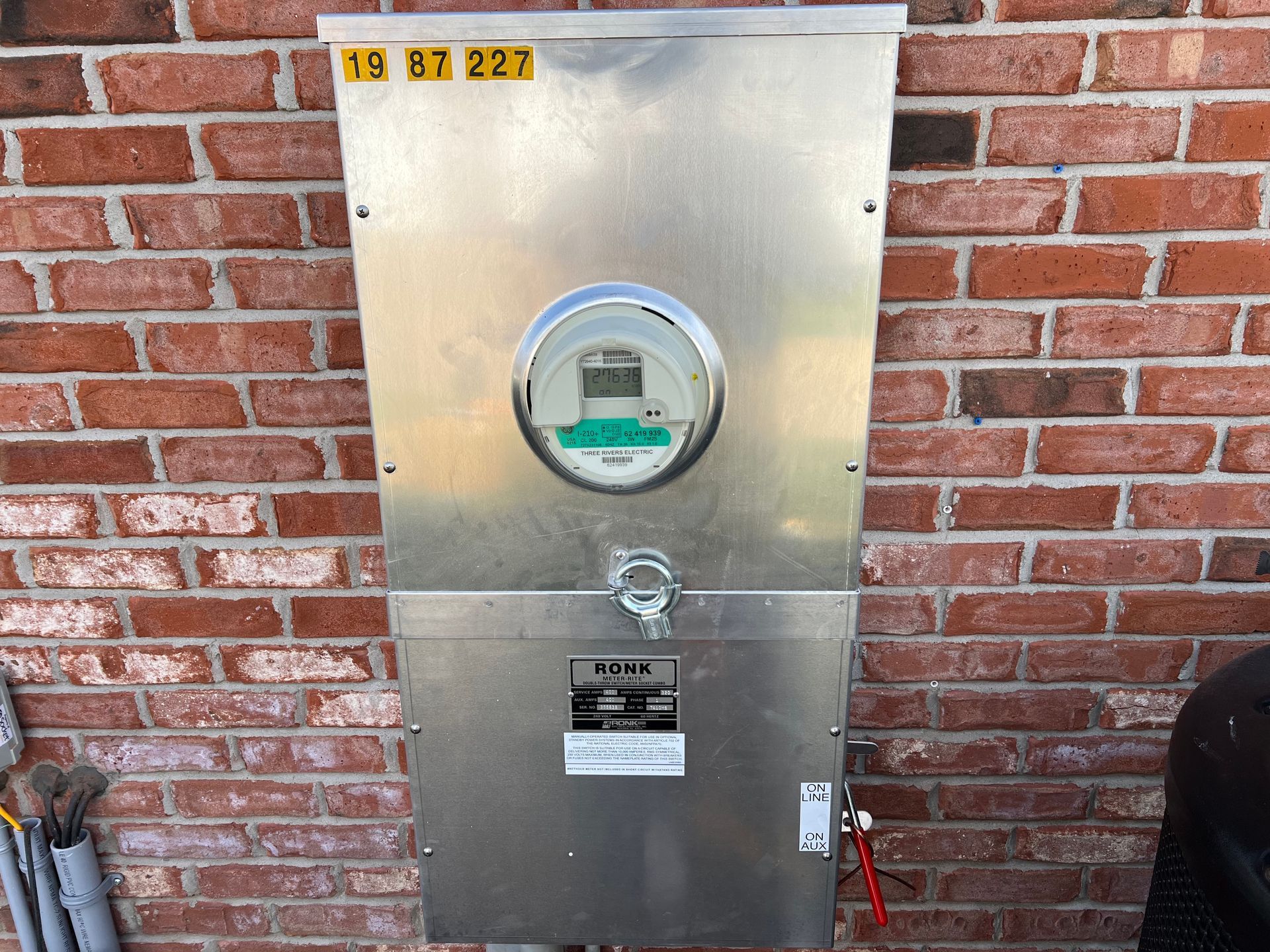 A stainless steel meter is mounted on a brick wall.