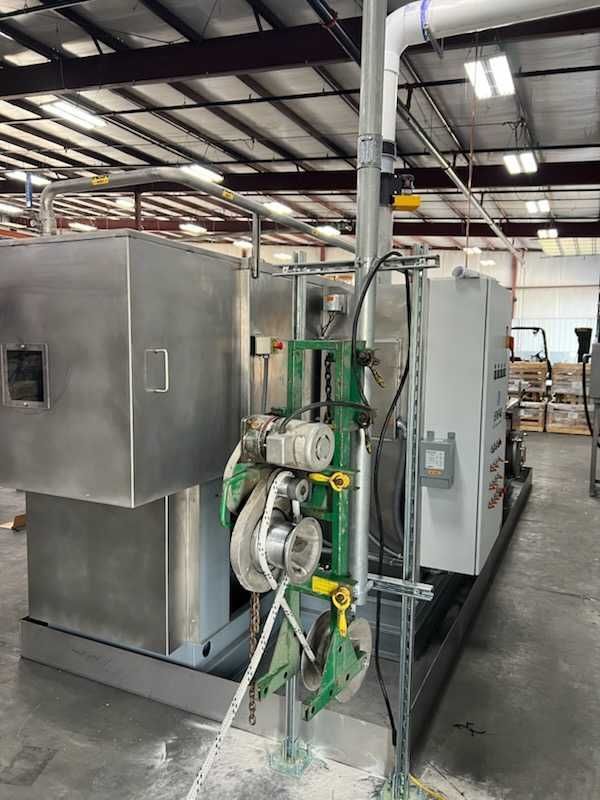 Industrial machinery with metal components and attached pipes inside a warehouse.