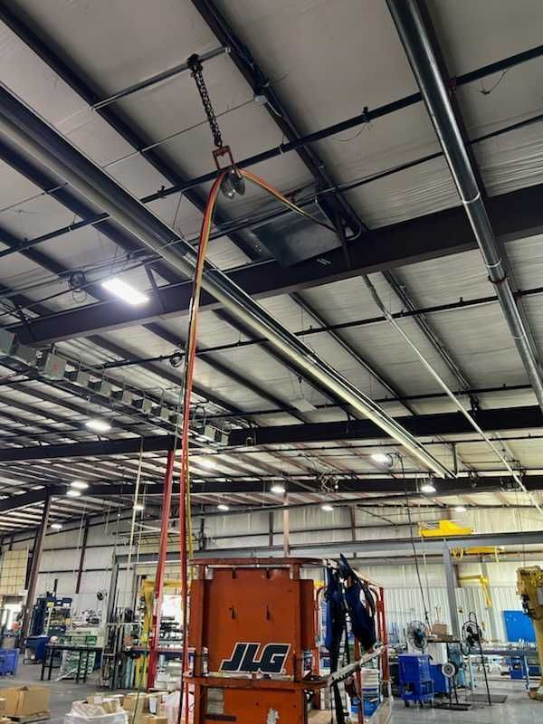 Orange lift truck with person operating, reaching for equipment overhead in industrial setting.