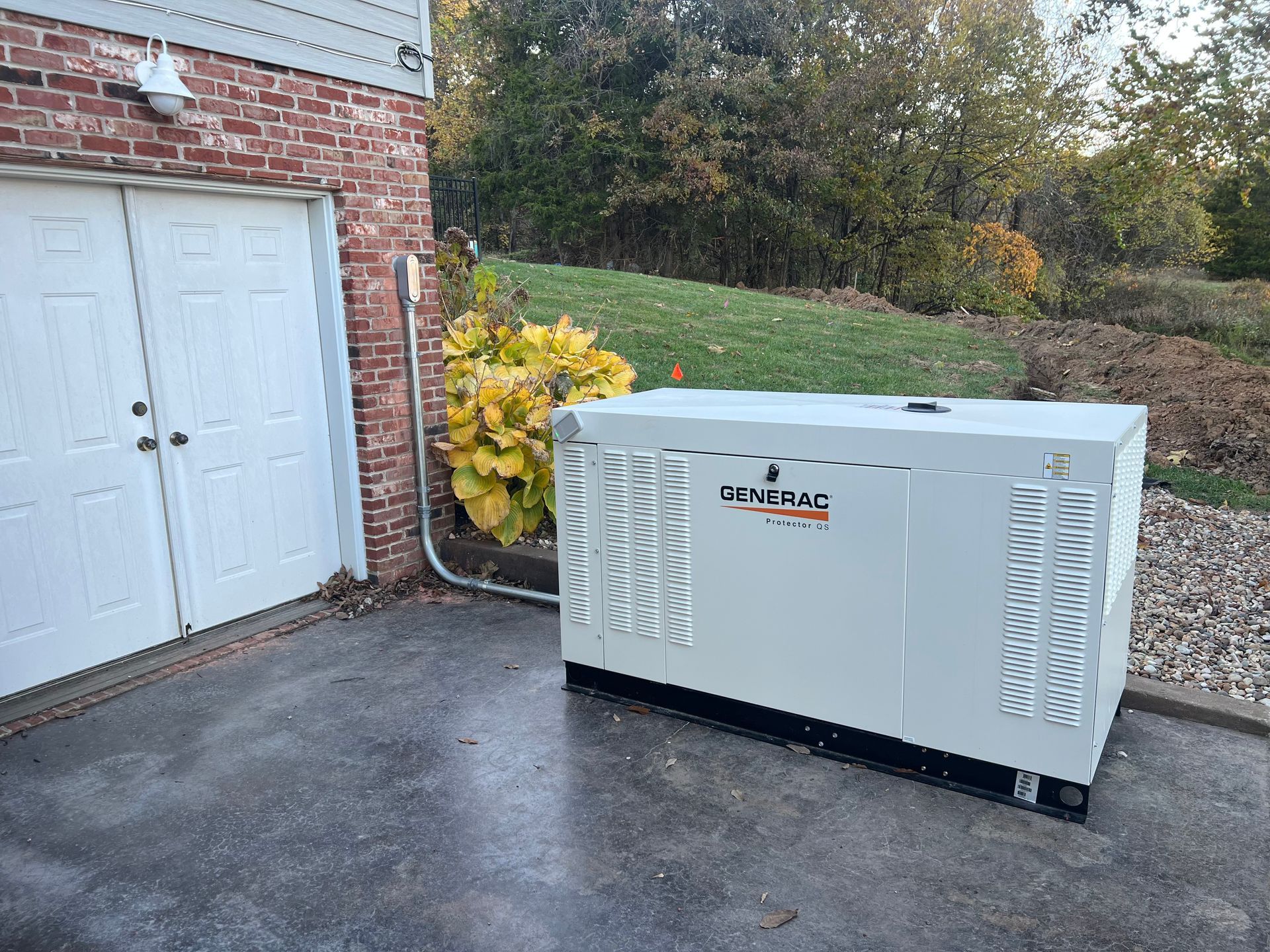 A white home generator next to a garage door on a concrete surface, with a brick wall backdrop.