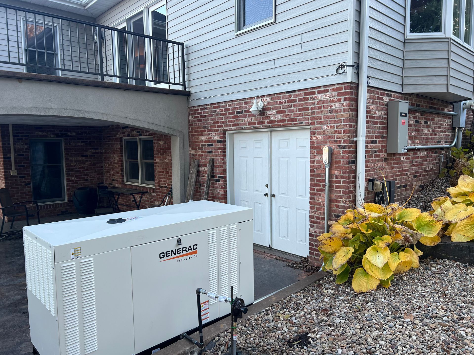 A large, white Generac generator is beside a house with a brick facade and white doors.