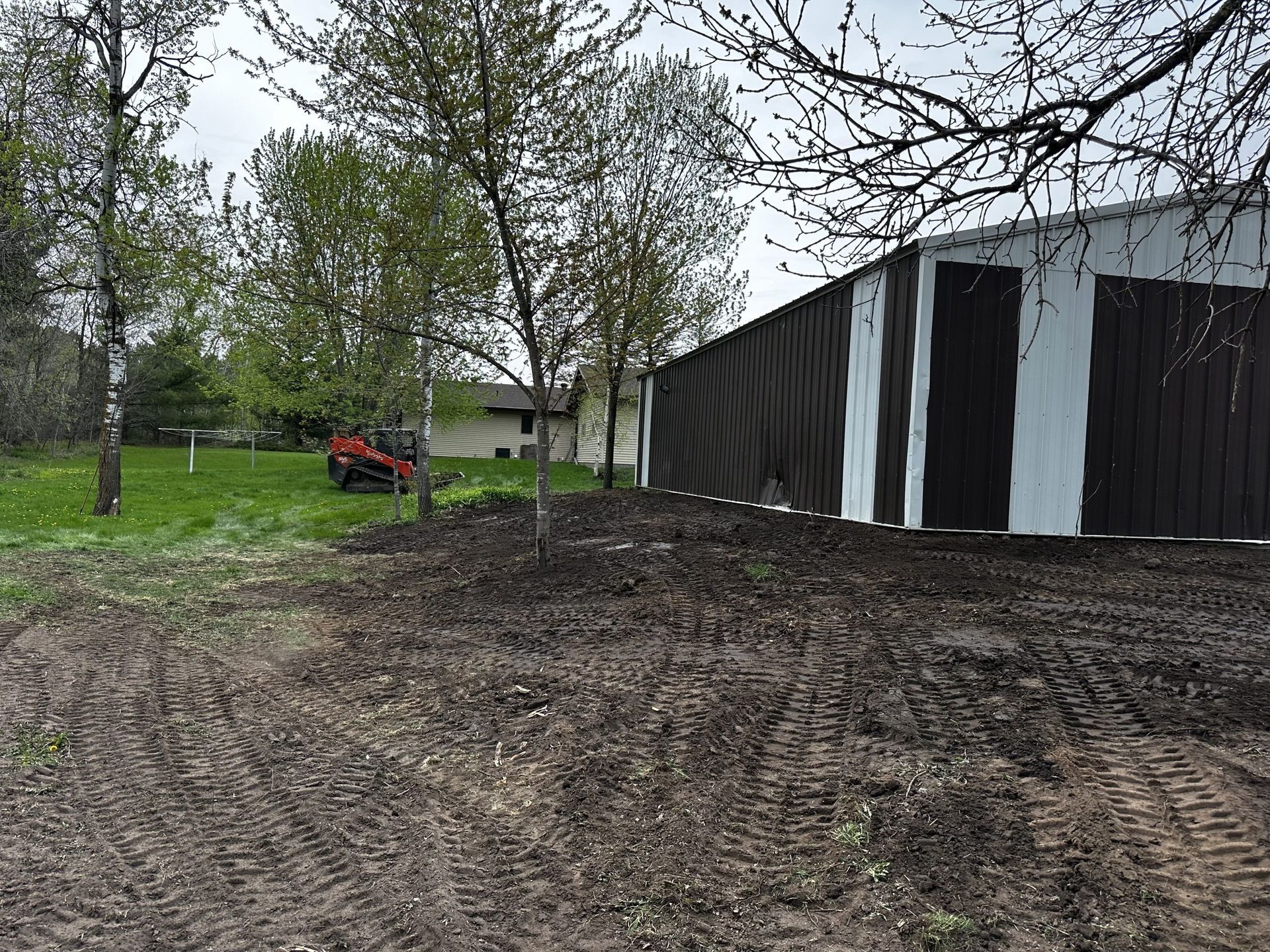 Dirt lot beside a black-and-white barn with trees and a small red tractor in the background