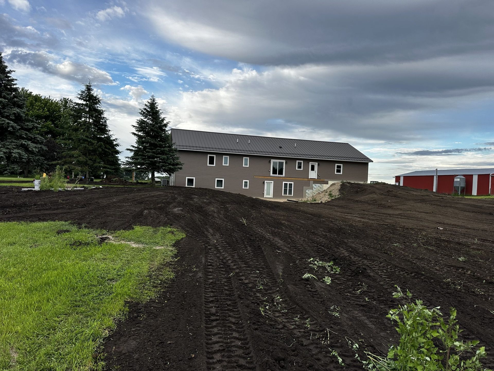 Grassy field beside a dirt lot and long beige building under a cloudy sky