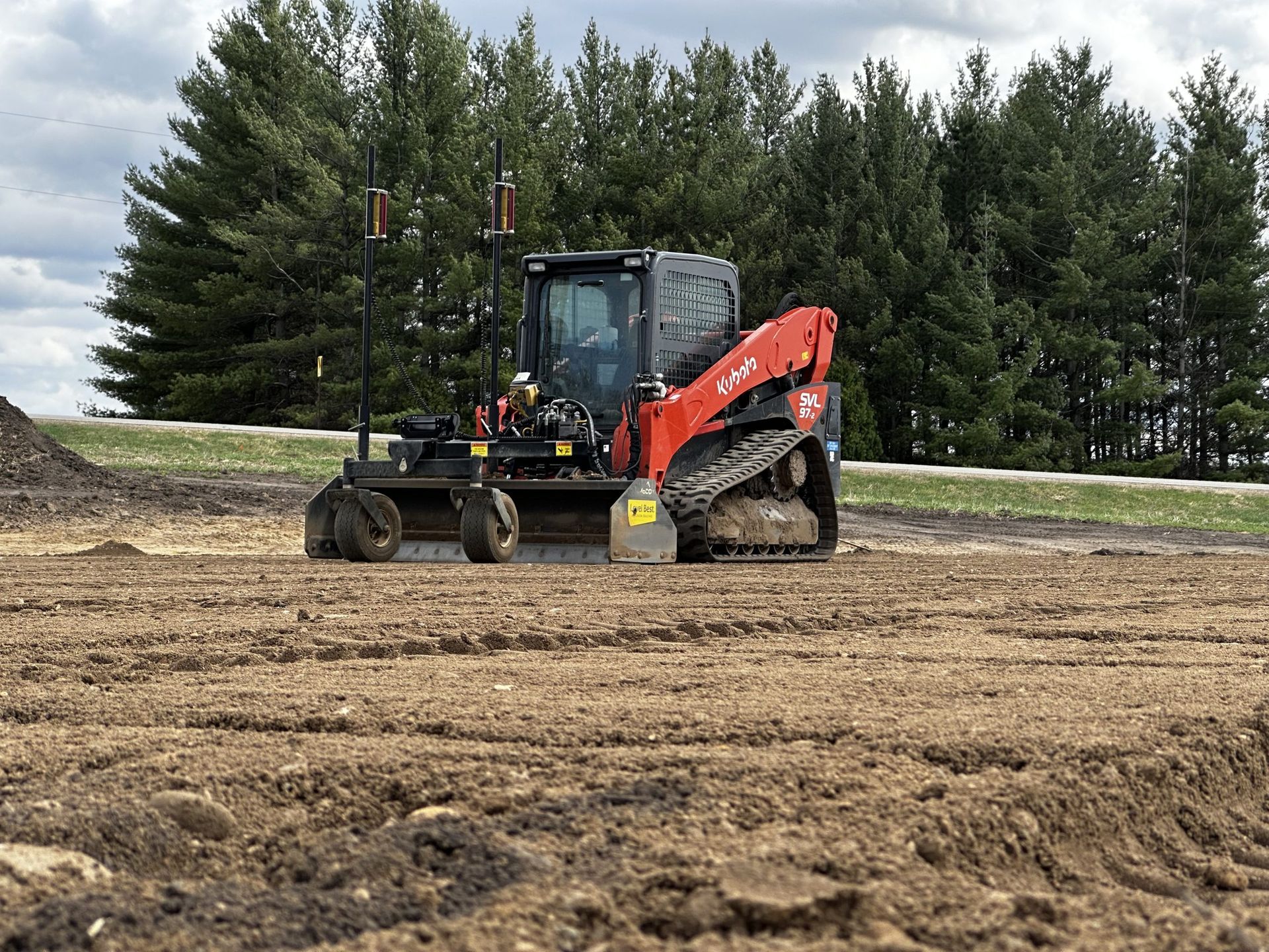 Orange excavator leveling dirt at a work site with trees in the background