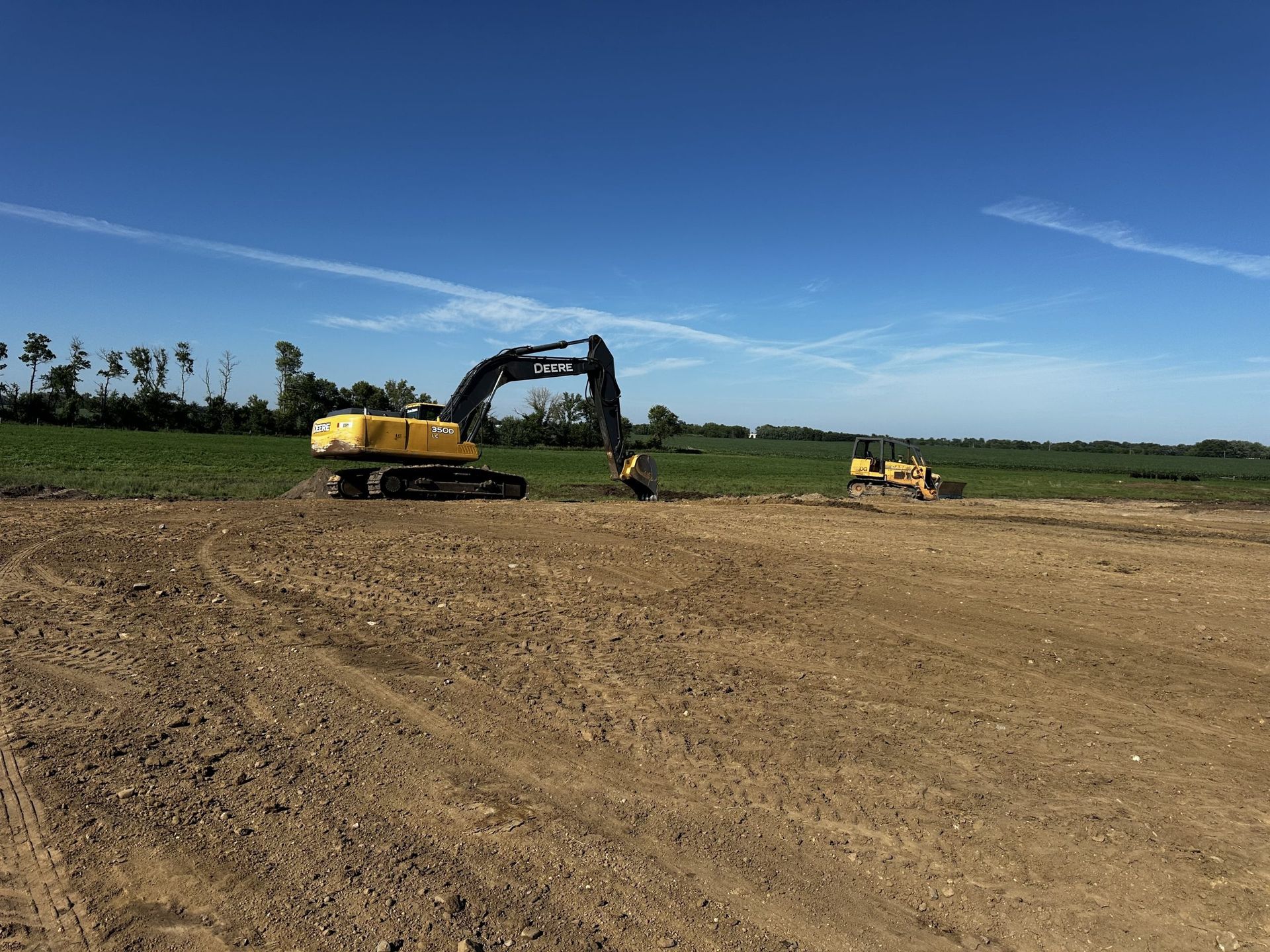 Excavator and bulldozer working on a dirt construction site under a clear blue sky