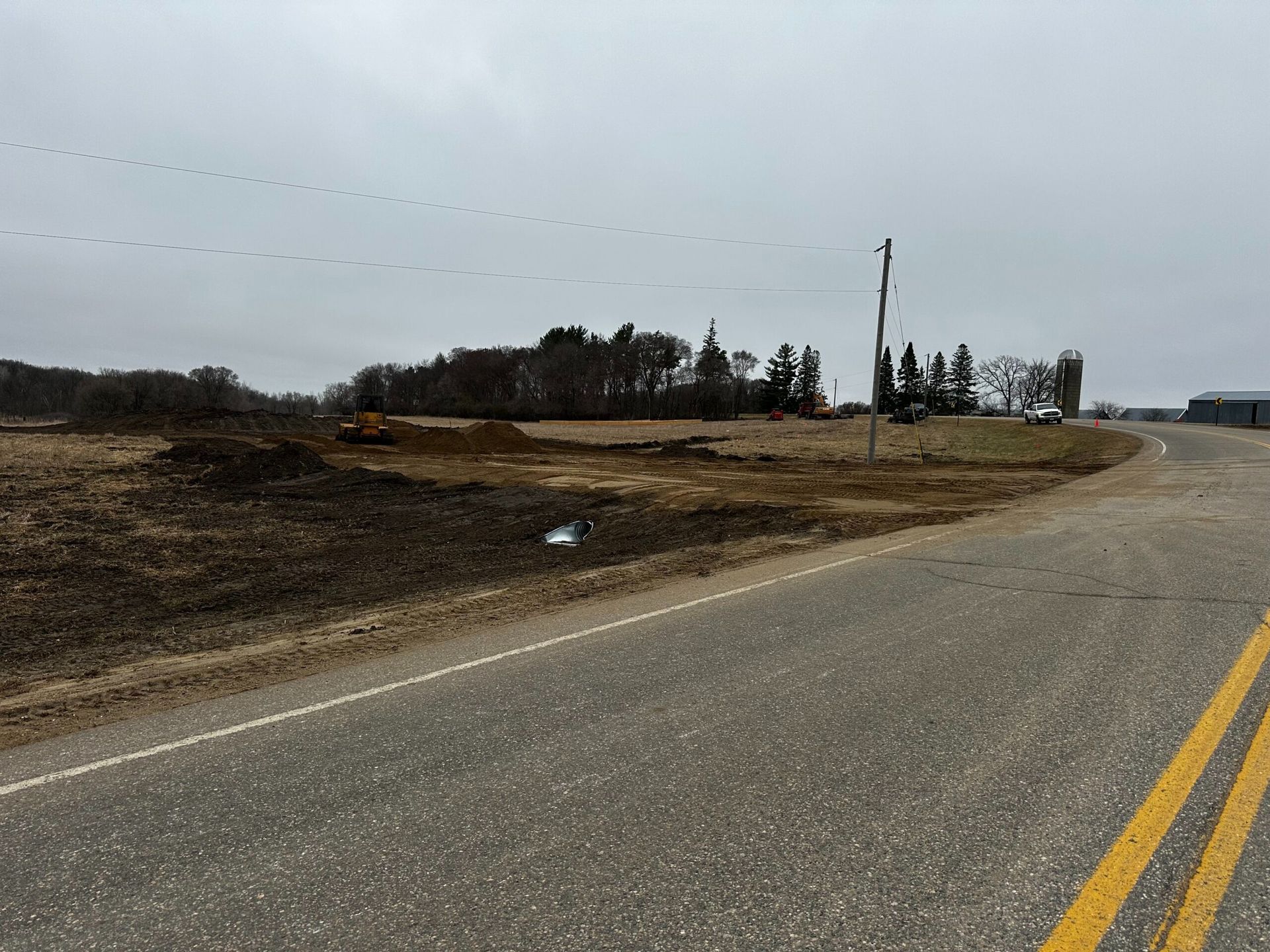 Empty rural road curving past barren fields and utility poles under an overcast sky