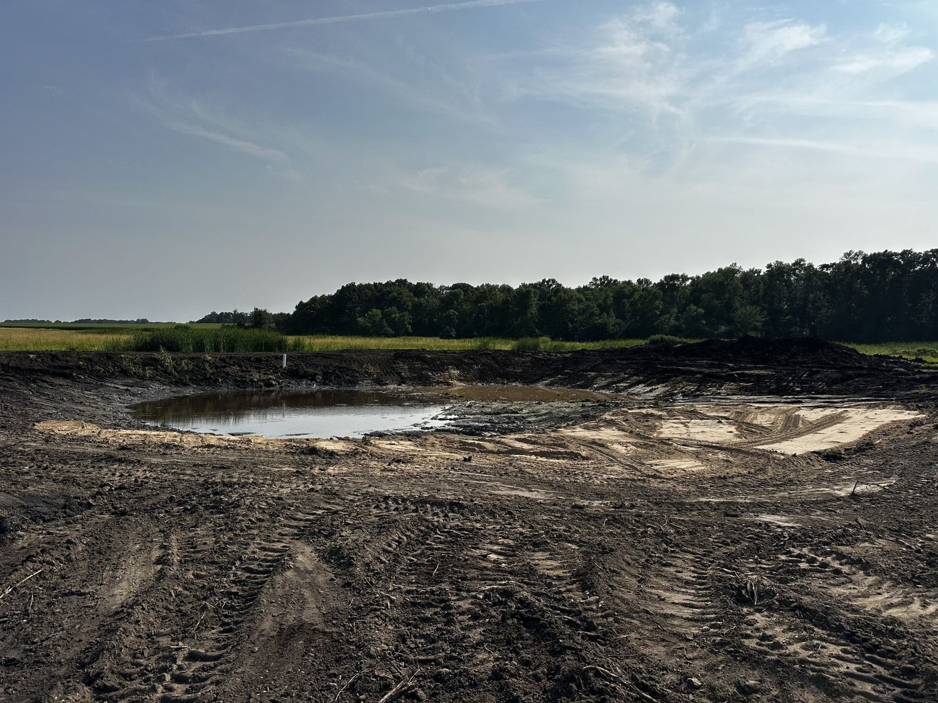 Mud-covered landscape with puddles, a tree line, and a cloudy sky