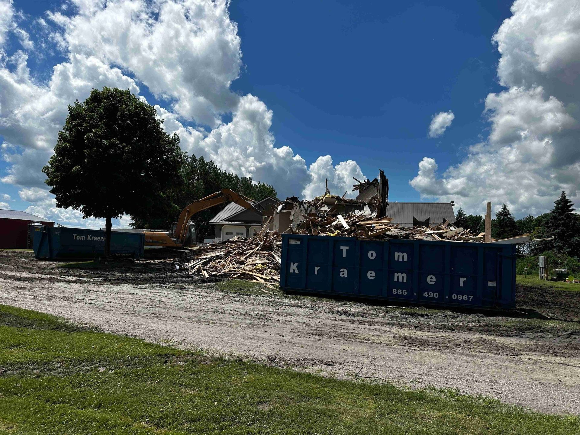 Demolition debris beside a blue dumpster under a cloudy sky on a dirt lot