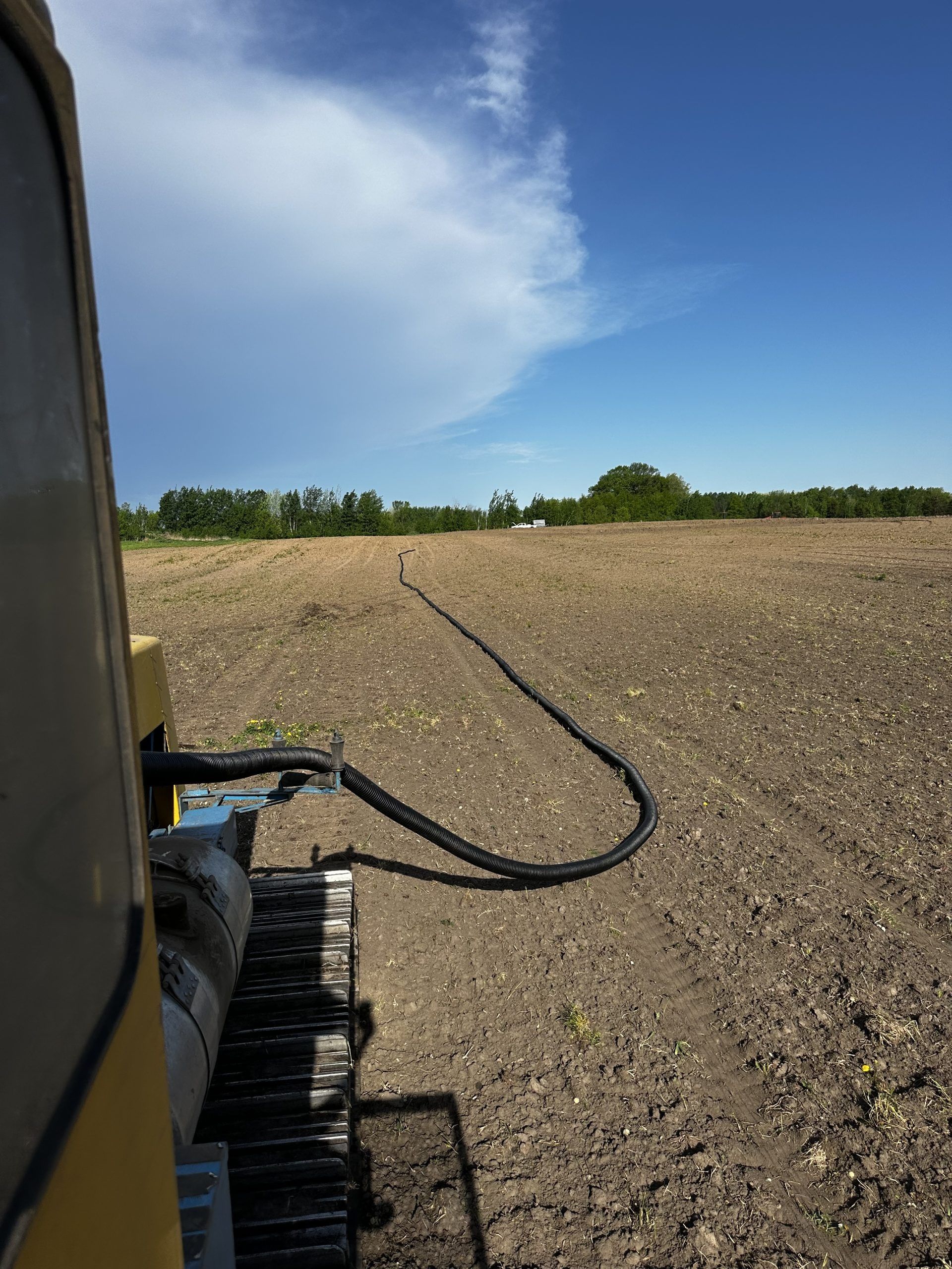 View from a farm machine over a freshly tilled field with a blue sky and distant tree line