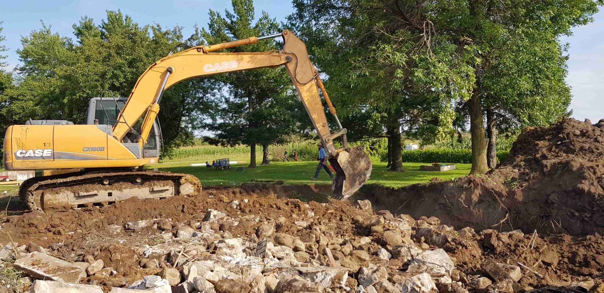 Yellow excavator digging through rubble in a wooded construction area