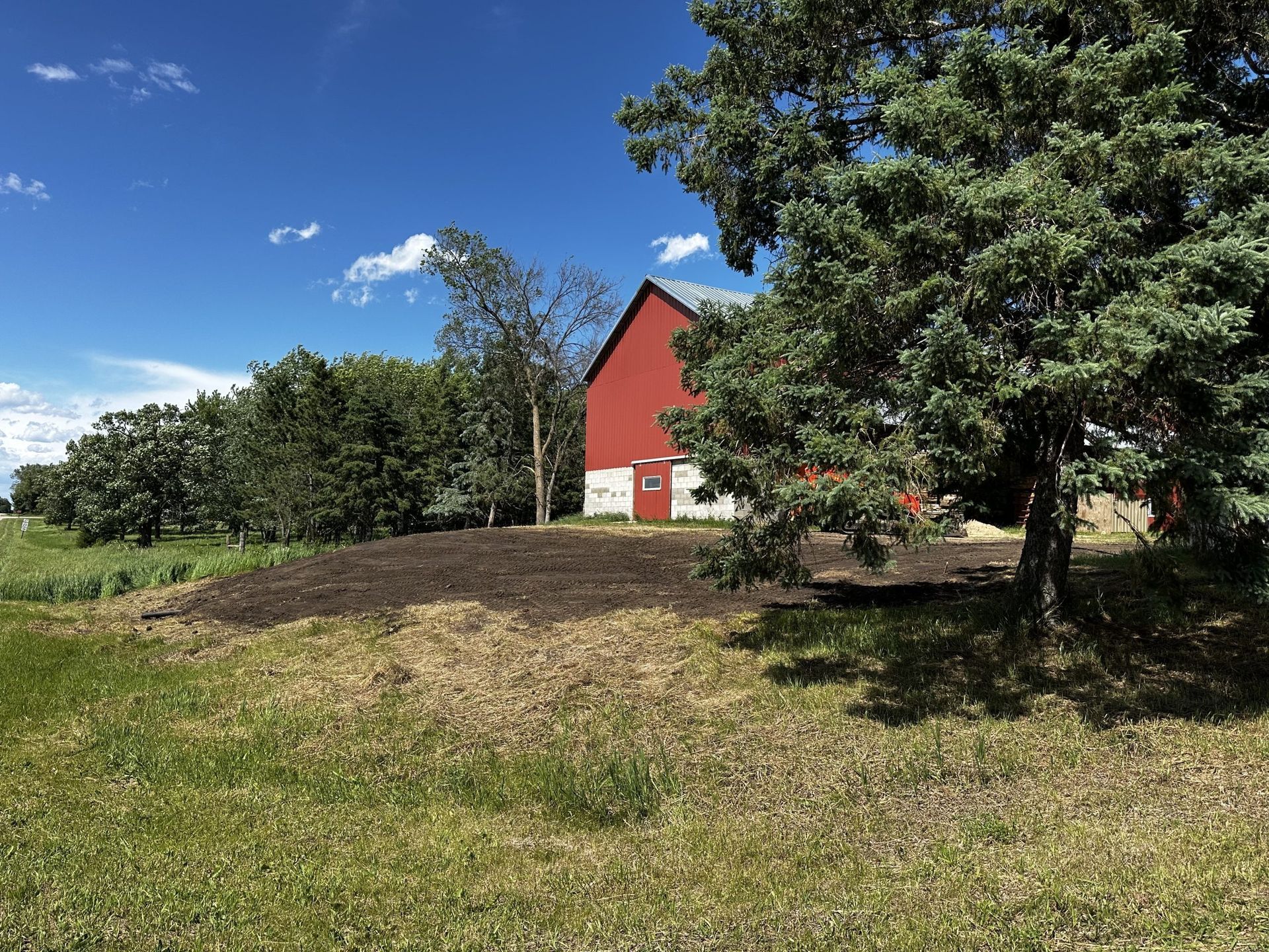 Red barn and trees on a grassy hillside under a blue sky