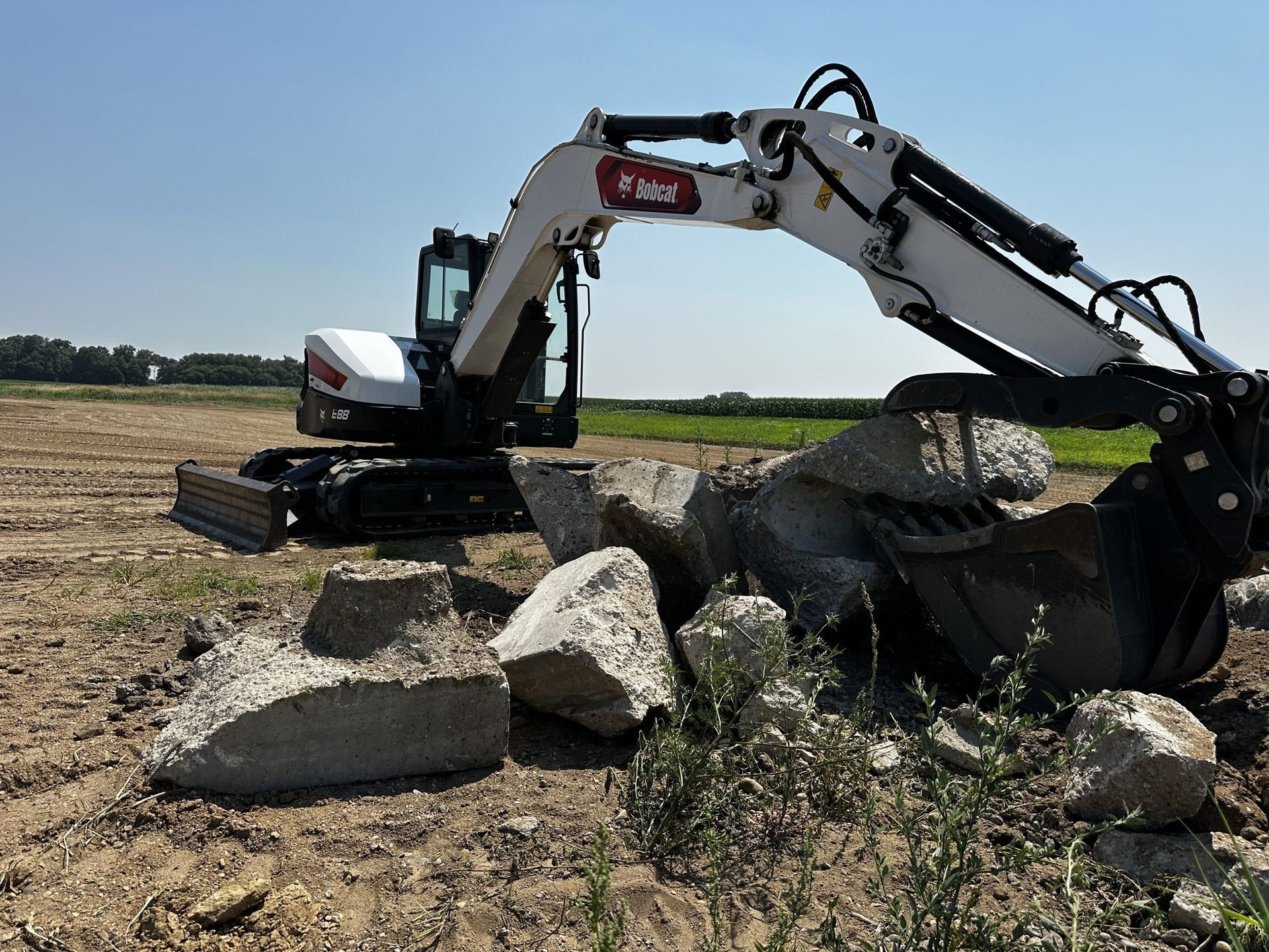 Excavator working beside large rocks in a field under a clear sky
