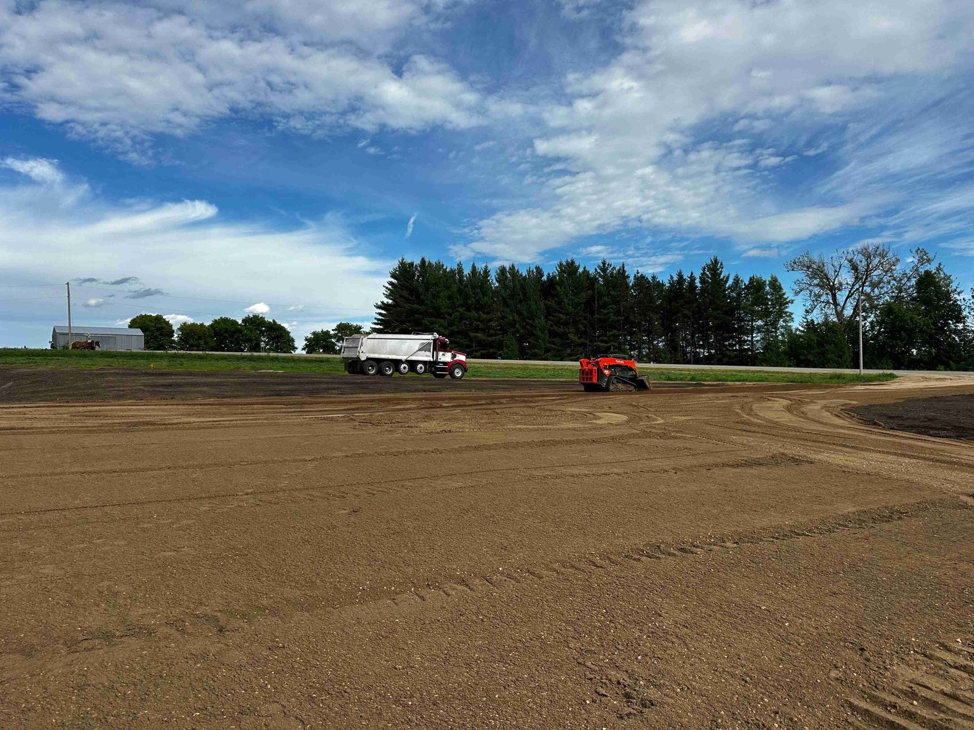 Tractor and white tanker truck on a plowed field under a blue sky