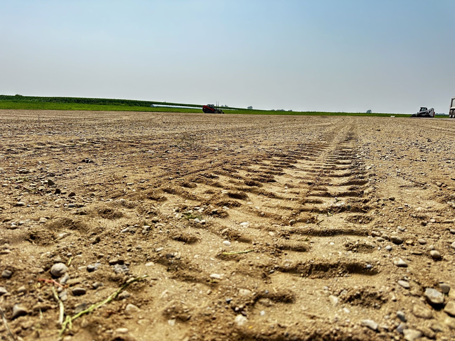Rutted dirt field under a clear sky with a green horizon line