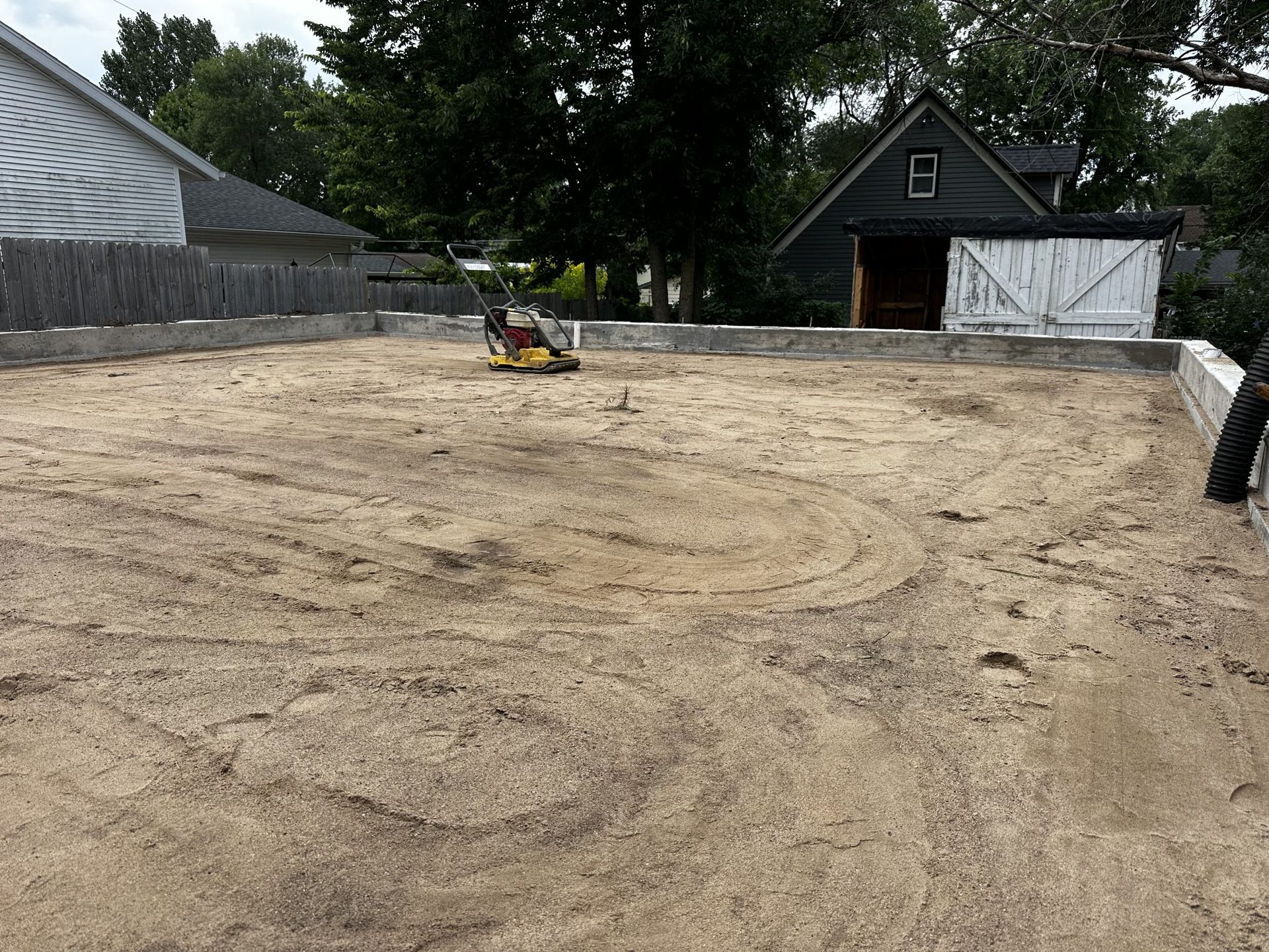 Gravel lot under construction with a compact loader and a house in the background.