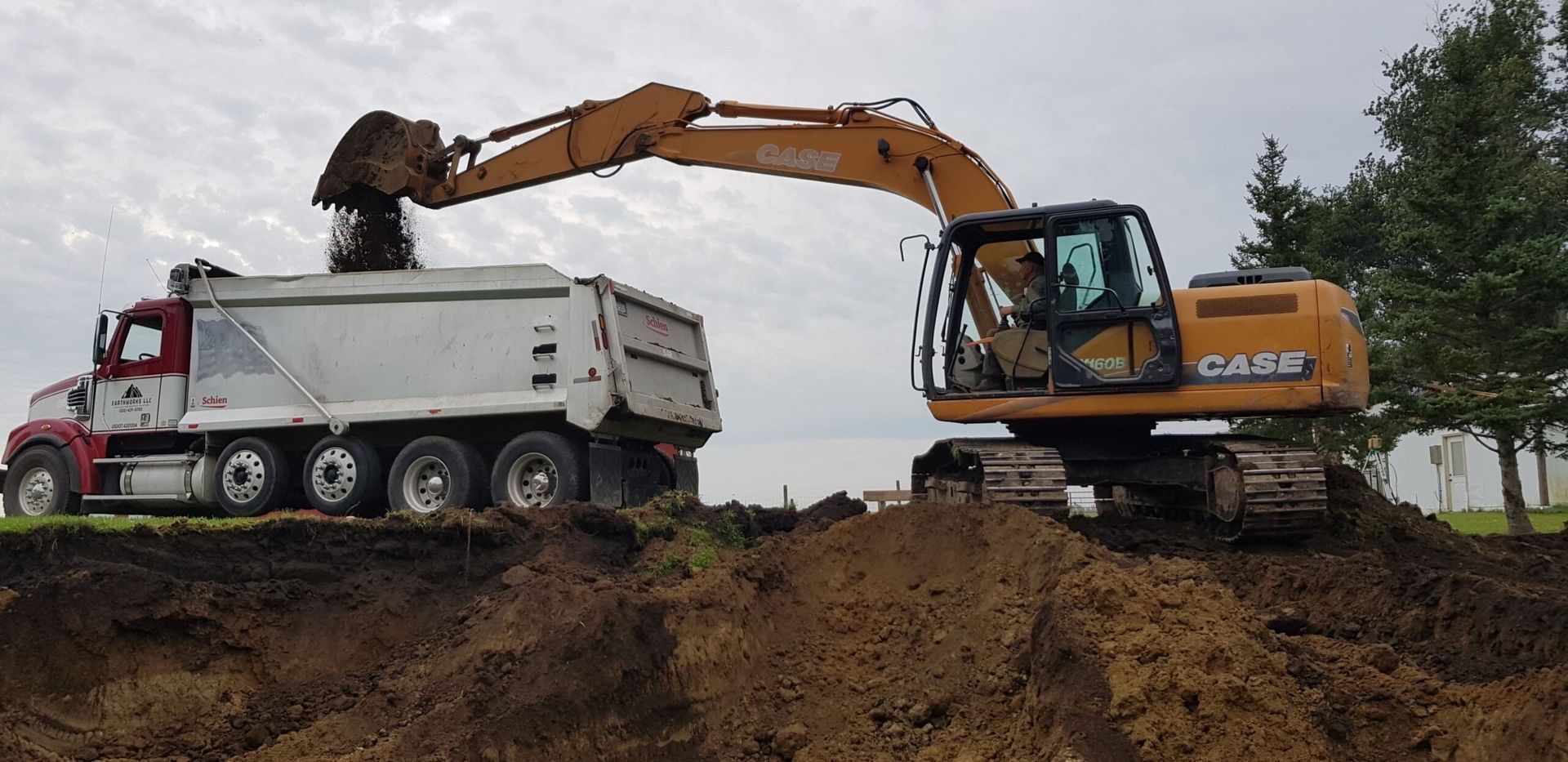 Orange excavator loading soil into white dump truck at a construction site